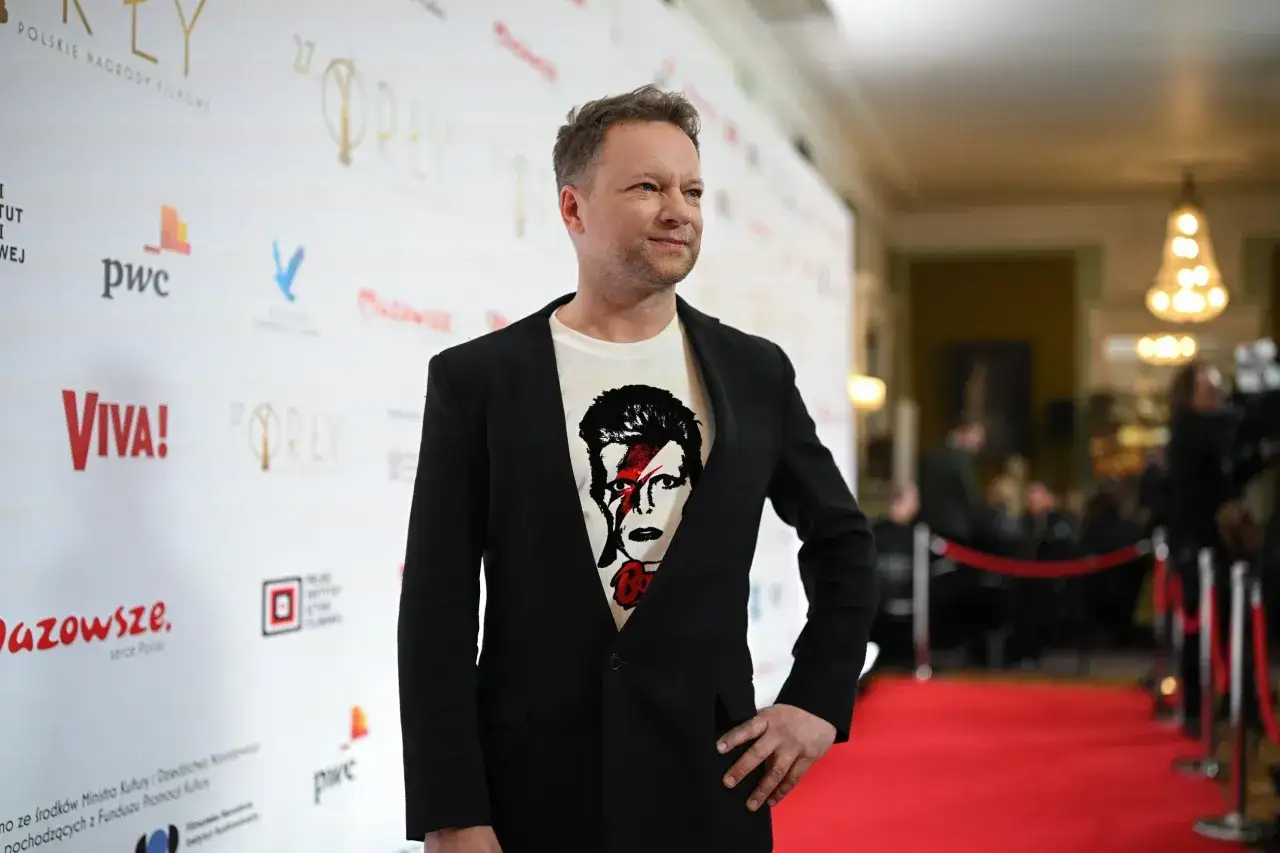 Polscy aktorzy na czerwonym dywanie. Mężczyzna w czarnej marynarce i t-shircie z wizerunkiem Davida Bowiego.