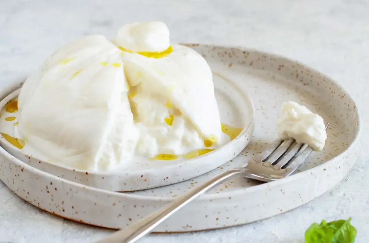 Puszysta burrata co to? Delikatny ser z płynnym wnętrzem, polany oliwą, na talerzu z widelcem.