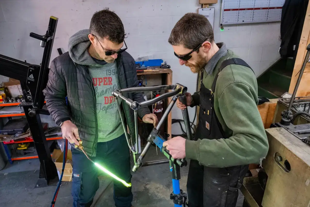 Two men, among the best custom bike builders, meticulously weld a bicycle frame in their workshop.
