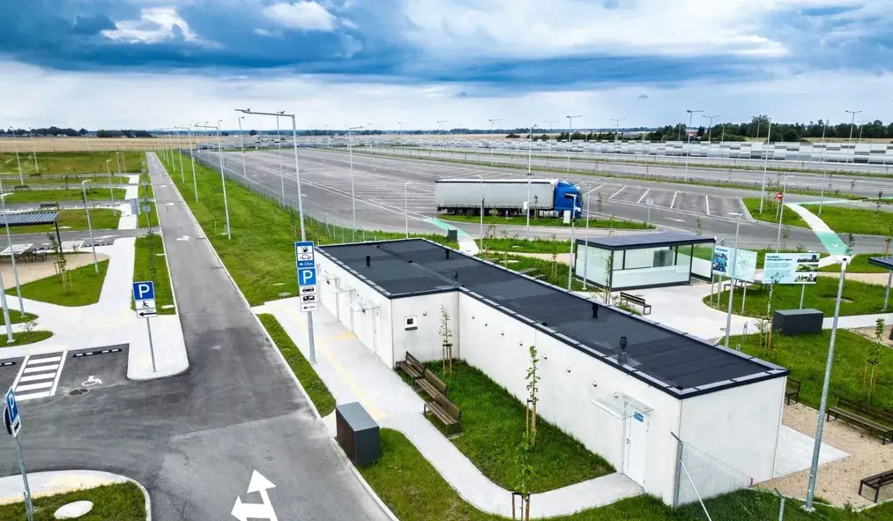 Nowy parking dla ciężarówek, część pakietu mobilności, zjazd na bazę. Widać budynek socjalny, ławki i duży plac manewrowy.