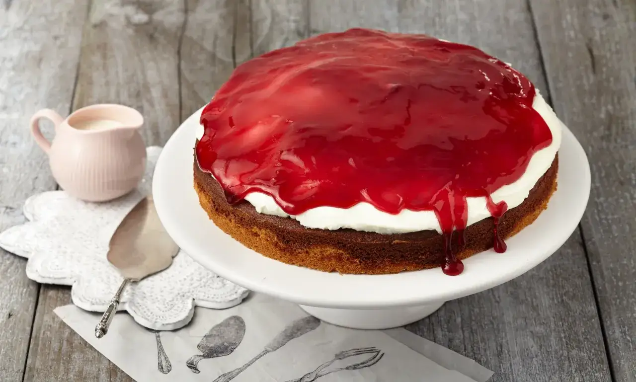 Eine köstliche Schneewittchen Torte mit weißer Sahne und glänzender roter Fruchtsauce, bereit zum Servieren.