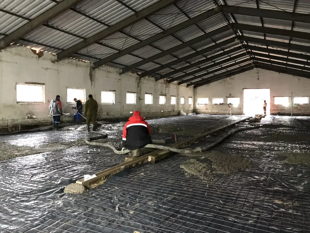 Pracownicy przygotowują podłoże pod wylewkę betonową, układając folię i zbrojenie w hali.