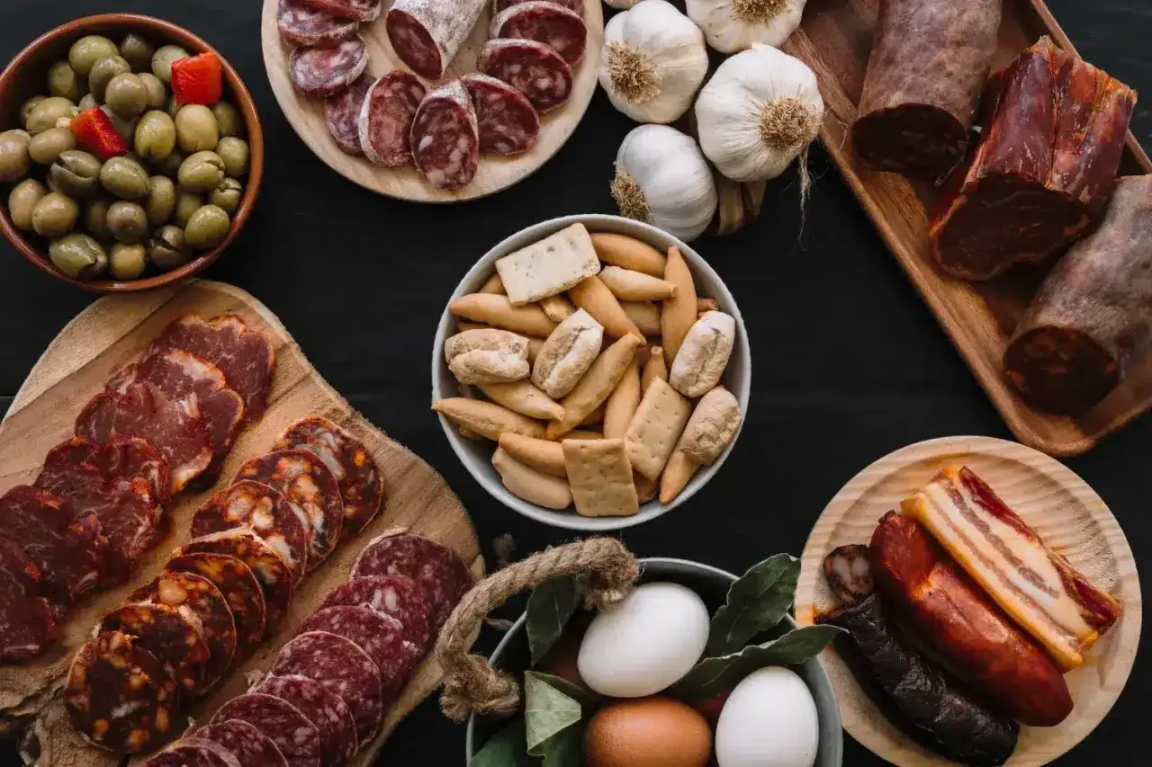 Una mesa repleta de delicias: qu&eacute; es charcuter&iacute;a, con embutidos variados, aceitunas, ajos, huevos y picos.