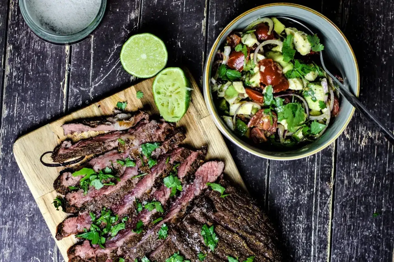 Perfekt gegrilltes Flank Steak, geschnitten und mit Koriander bestreut, neben einem frischen Avocado-Tomaten-Salat. Ein tolles Flank Steak Rezept für den Sommer.