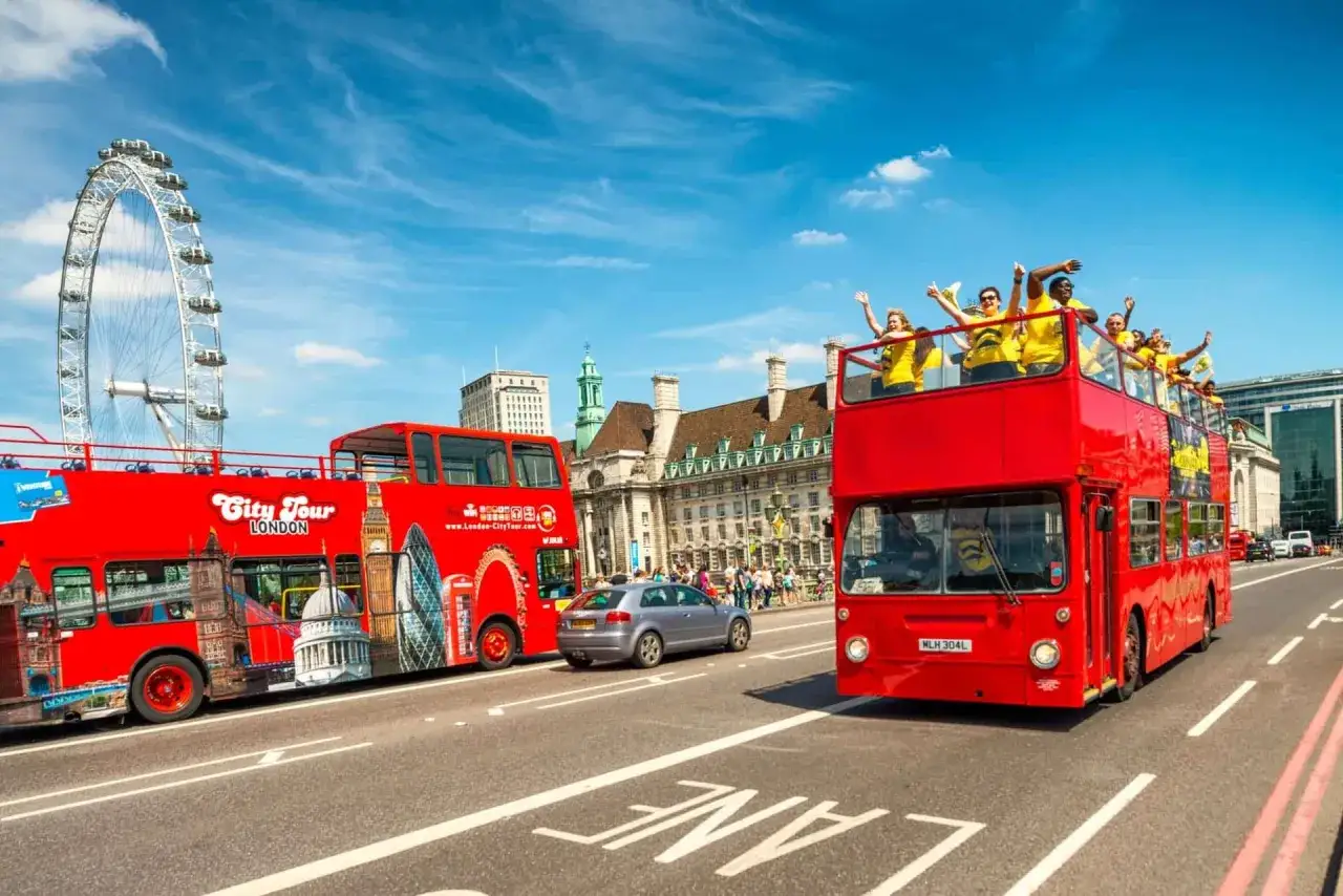 Czerwony autokar do Londynu z turystami na piętrze, obok London Eye i zabytkowych budynków.