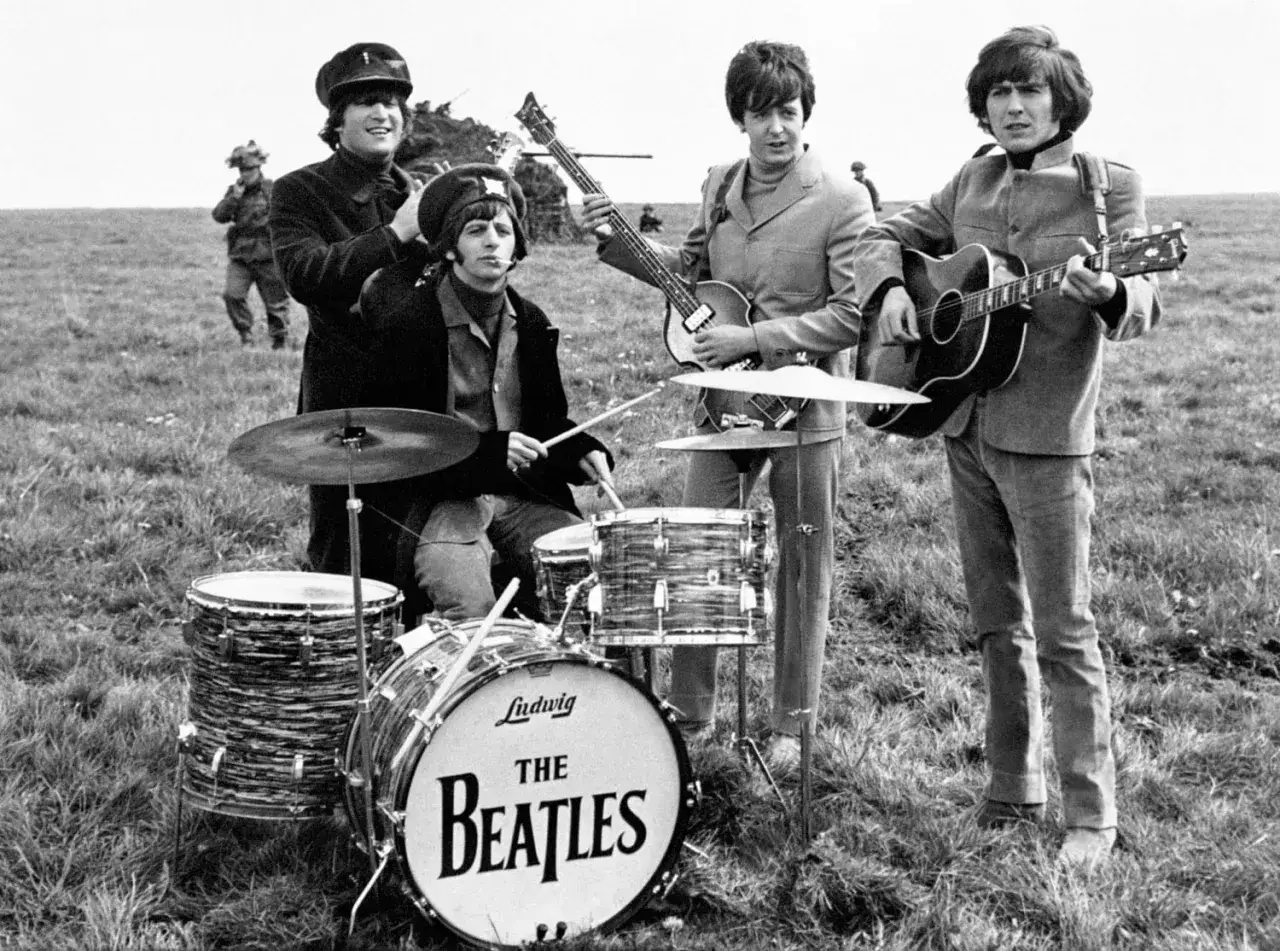Les Beatles jouent en plein air. Ringo frappe la batterie, John et Paul jouent de la guitare, George est aussi présent.