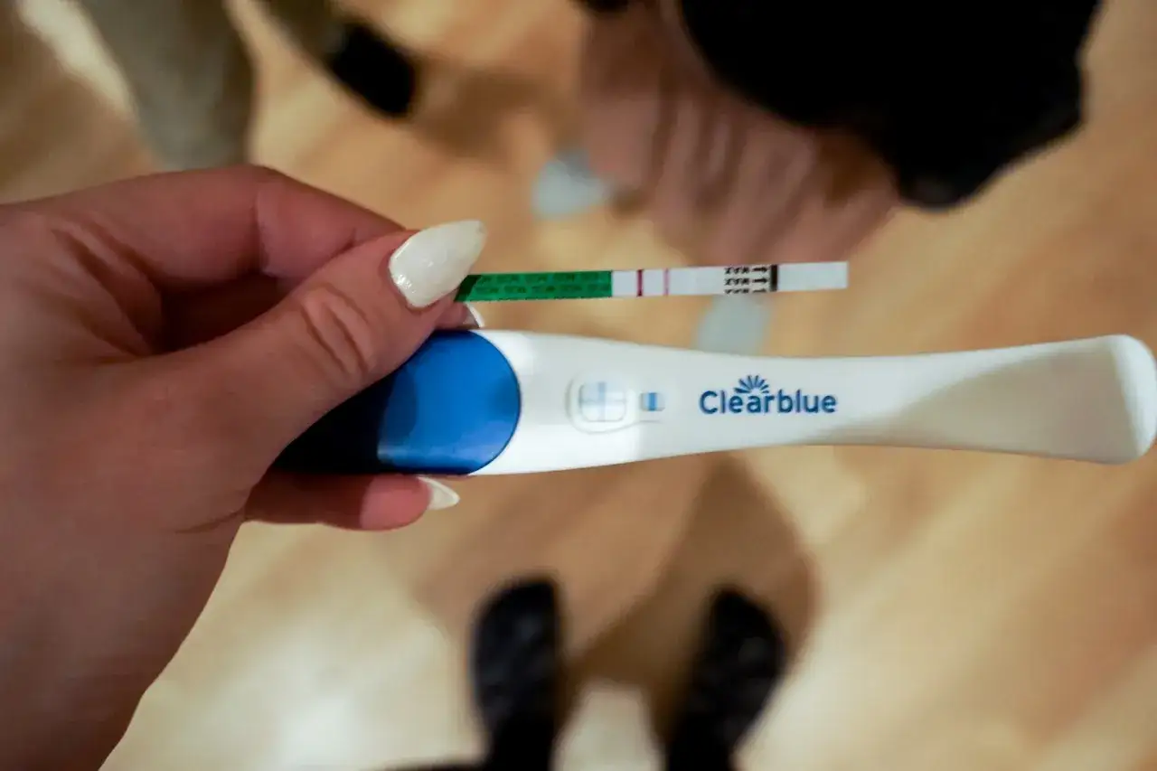 Gravid trots negativt test v 7. En hand håller upp två graviditetstest. Ett visar ett svagt positivt resultat, det andra ett negativt.