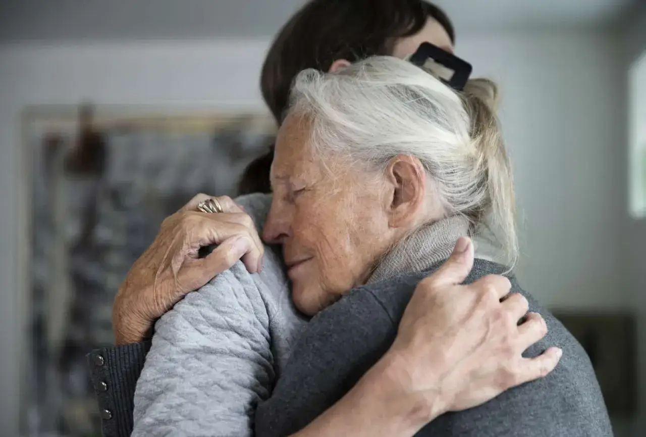 Zwei Frauen umarmen sich innig. Die &auml;ltere Frau schlie&szlig;t die Augen, w&auml;hrend sie Trost findet. Die Alzheimer Lebenserwartung ist ein wichtiges Thema.