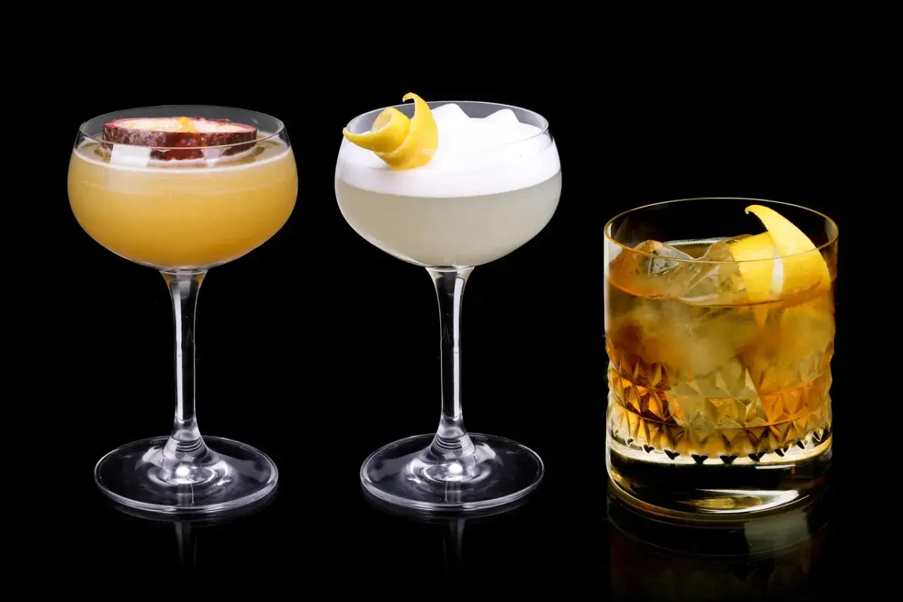 Trzy drinki: żółty z marakują, biały z pianką i cytrynową skórką, oraz bursztynowy z lodem i skórką cytryny. Ten ostatni, z dodatkiem triple sec, kusi.