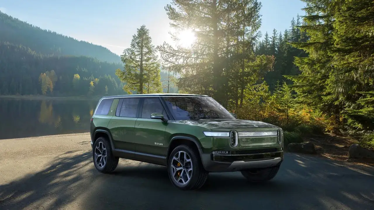 Un SUV elettrico verde, uno dei nuovi suv elettrici, si ferma su una strada sterrata vicino a un lago e una foresta.