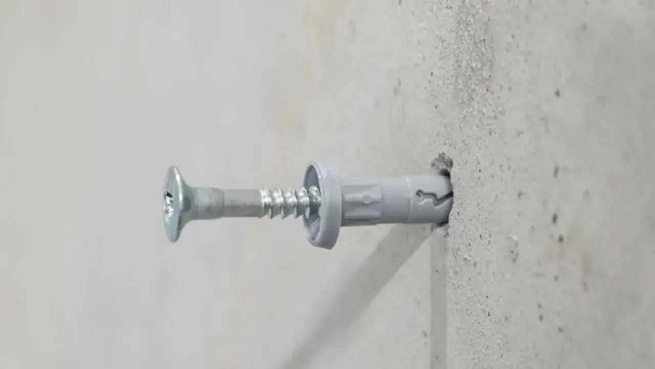 Kołki rozporowe do regipsu, wkręcone w betonową ścianę, zapewniają solidne mocowanie.