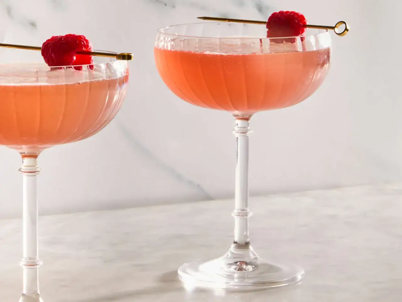 Tv&aring; eleganta glas med rosa drink, en klassisk french martini, toppad med f&auml;rska hallon p&aring; en guldig spett.