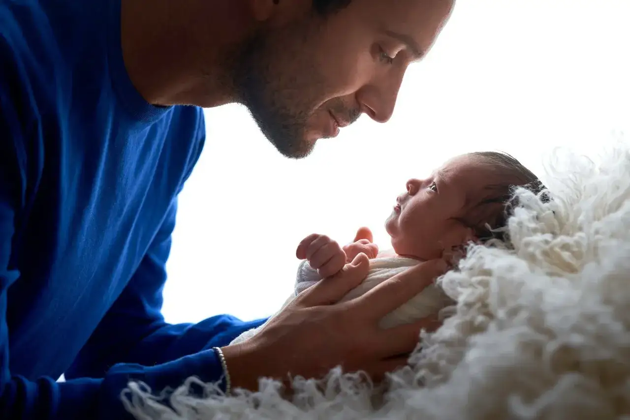 Padre innamorato guarda il suo neonato avvolto in una coperta soffice. Momenti preziosi di immagini neonati.