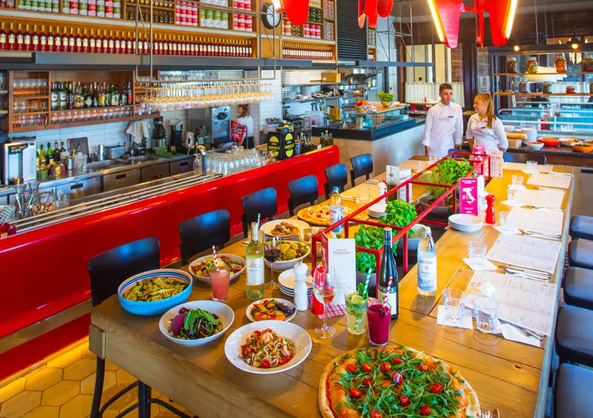 Pyszne jedzenie i napoje na stole w restauracji Otto Pompieri. W tle bar z pracownikami.
