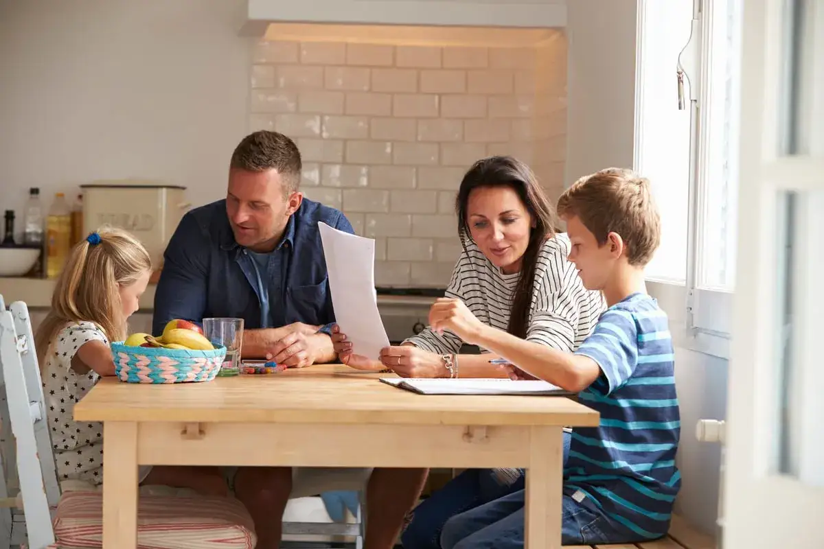 Familia reunida en la mesa, aprendiendo juntos. Los padres guían a sus hijos, aplicando los principios de la disciplina positiva para fomentar el aprendizaje y la conexión.