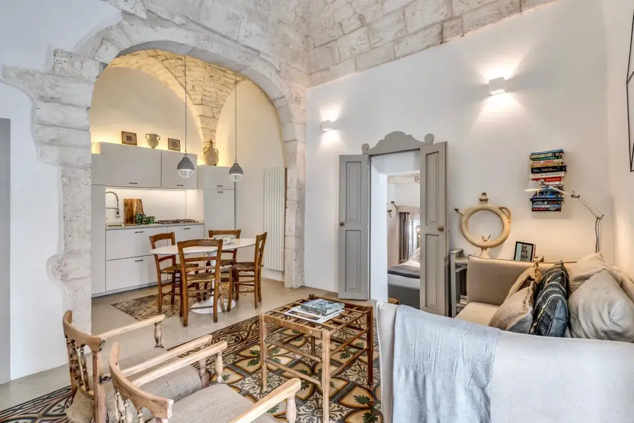 Un soggiorno moderno con un suggestivo arco in pietra che collega la zona giorno alla cucina. Pavimenti decorati e arredi in legno creano un'atmosfera accogliente.