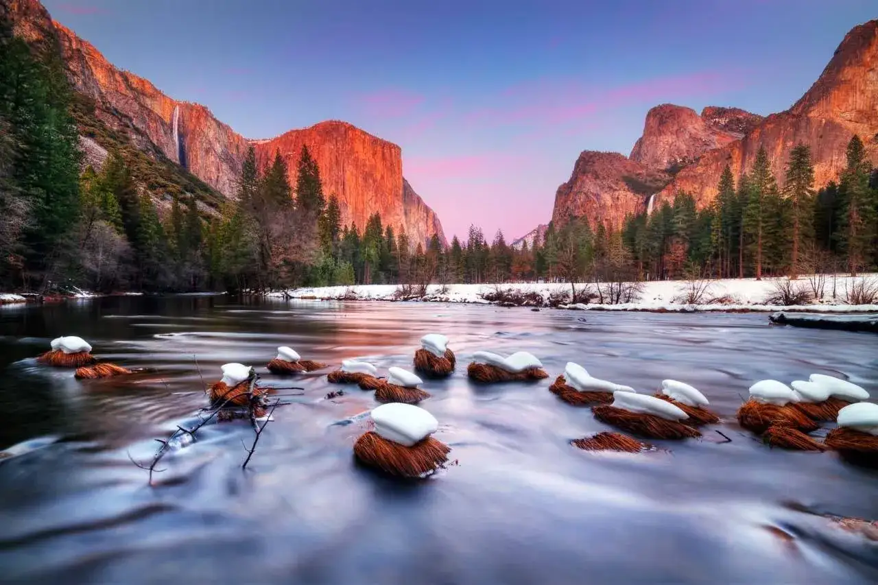 Zimowy świt w Yosemite, jednym z najpiękniejszych parków narodowych USA. Rzeka płynie wśród ośnieżonych skał, a góry mienią się w blasku wschodzącego słońca.