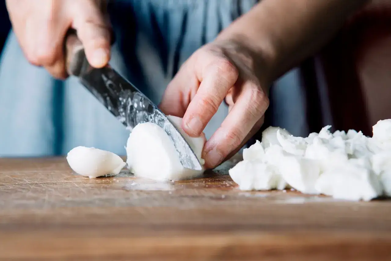 Ręce kroją białą mozzarellę na desce. Zastanawiasz się nad mozzarella kcal?