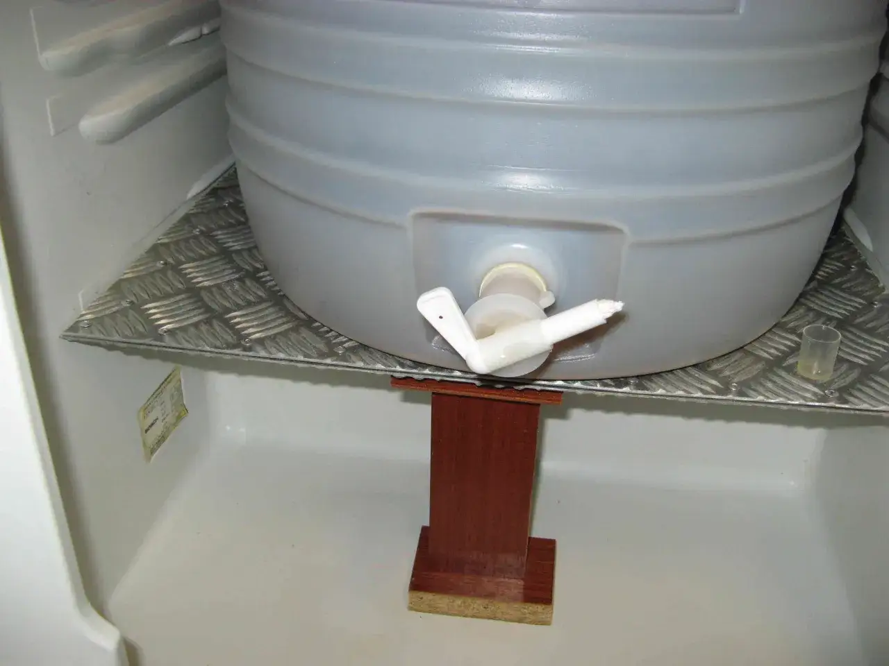 Un grand récipient de bière en cours de cold crash dans un réfrigérateur, sur une étagère en métal.