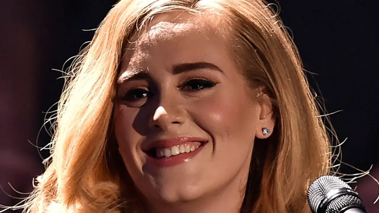 Uśmiechnięta Adele, z blond włosami i błyszczącymi ustami, gotowa do zaśpiewania. hello adele tekst.