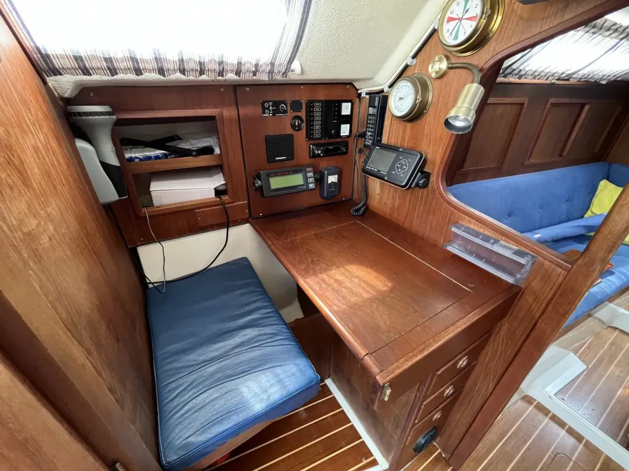 Gemütliche Navigationsecke auf der Comfortina 32 mit Holztisch, blauem Sitzpolster und Navigationsinstrumenten.