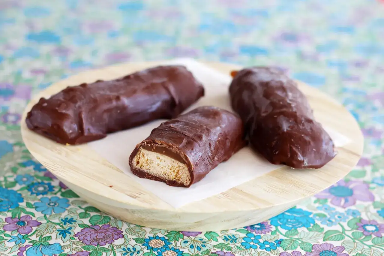 Trois délicieux mikados maison enrobés de chocolat noir, présentés sur une assiette en bois.