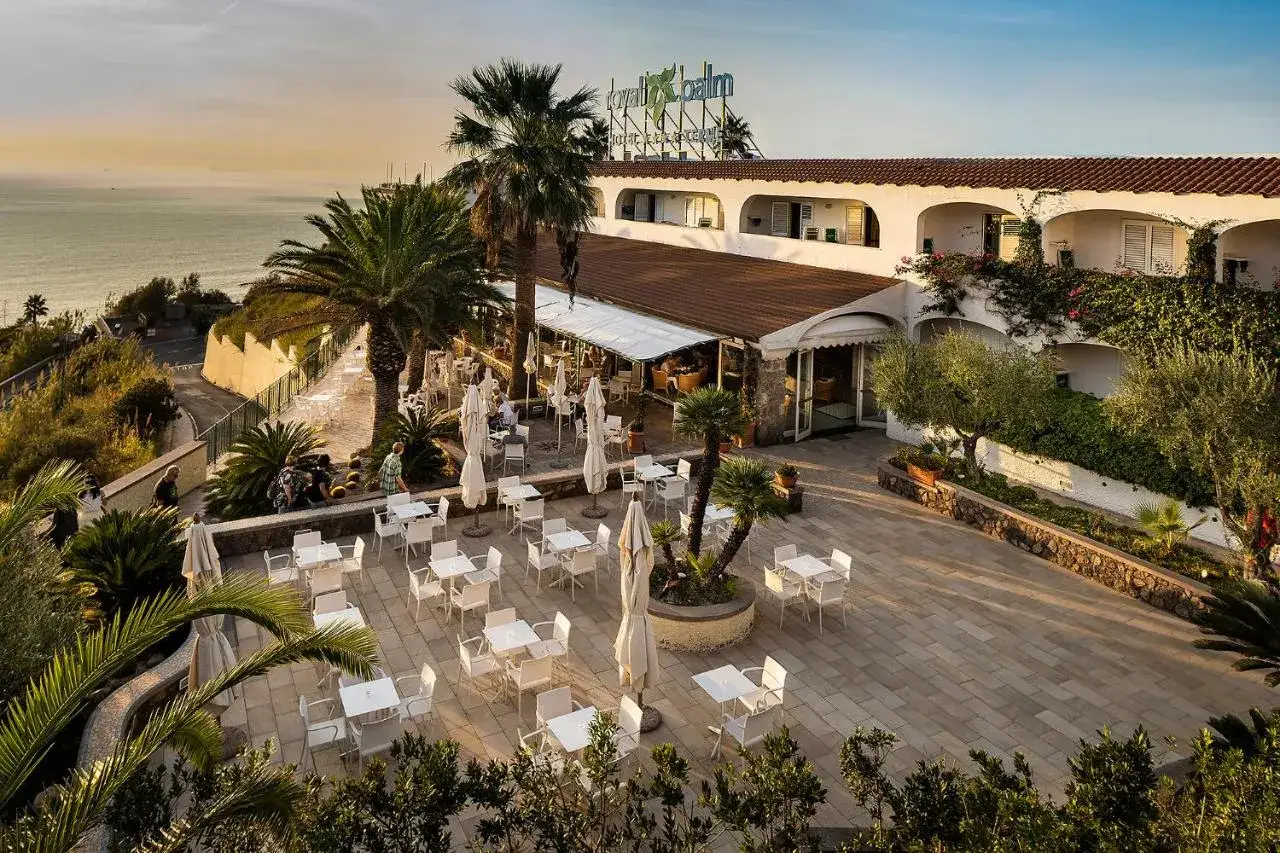 Terrazza con tavoli e sedie all'aperto del **hotel Le Palme Ischia**, con vista sul mare al tramonto e palme rigogliose.