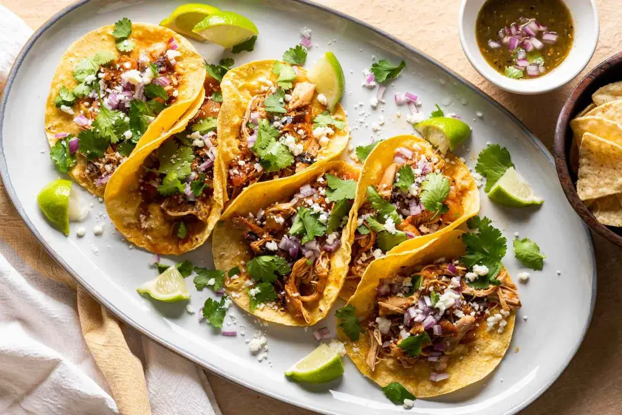 En tallrik med fem kycklingtacos, toppade med koriander, lök och ost. Serveras med limeklyftor och en skål salsa. Perfekt för ett snabbt tacos recept.