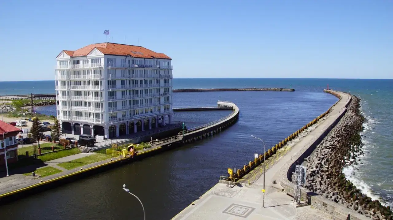 Nowoczesny budynek Marina Royale nad kanałem w Darłówku Wschodnim, z falochronem prowadzącym do morza.