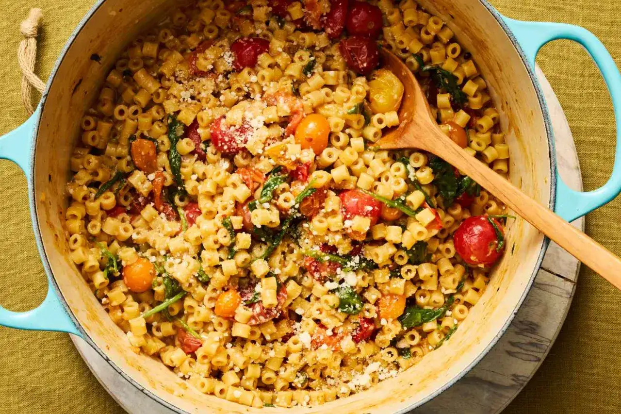 Un plat de pâtes d'une seule casserole, garni de tomates cerises, d'épinards et de parmesan râpé, prêt à être servi.