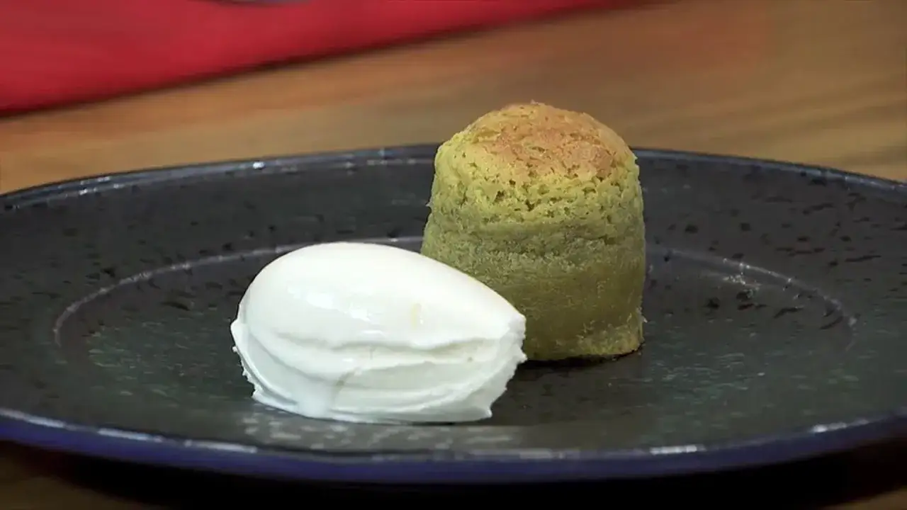 Coulant de pistacho verde, esponjoso y con una bola de helado blanco cremoso, servido en plato oscuro.