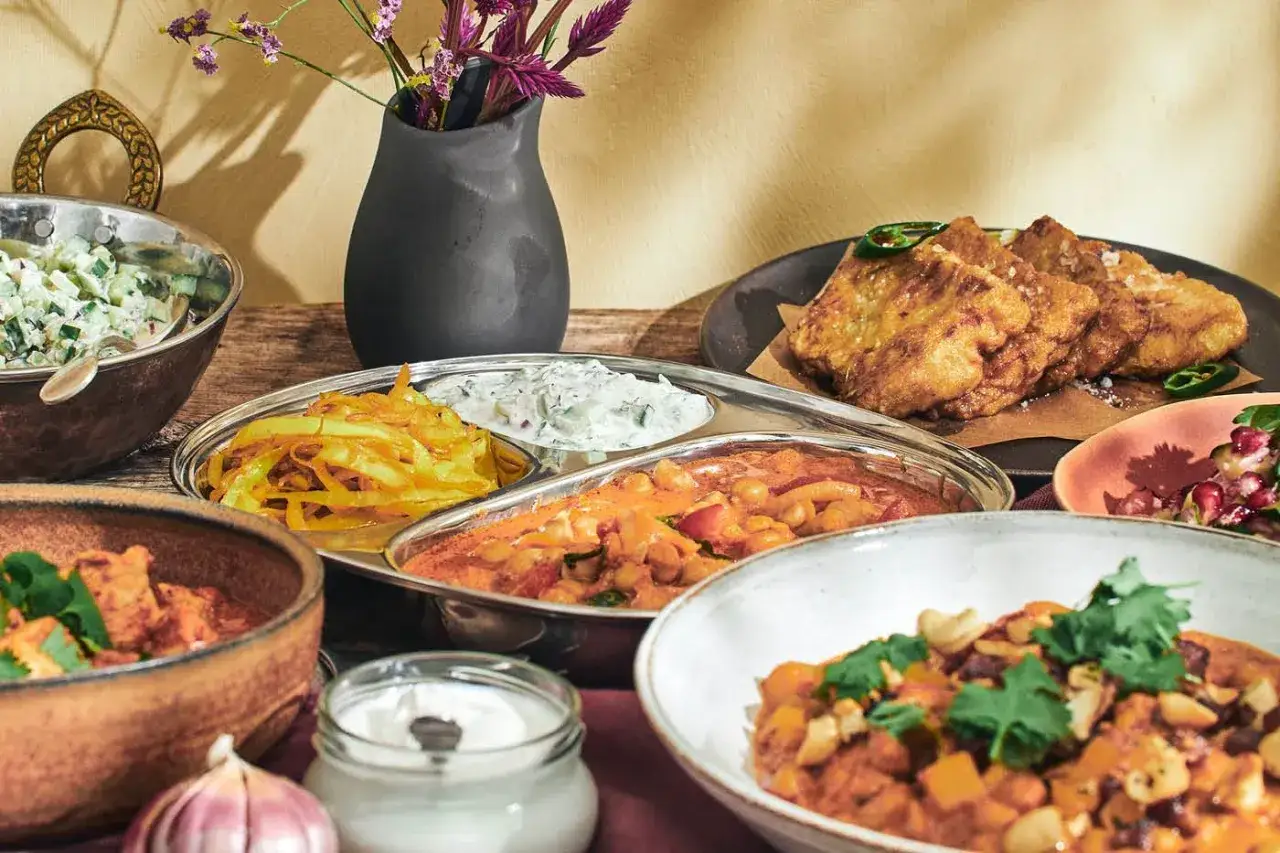 En festlig dukning med olika r&auml;tter av indisk mat, inklusive curry, raita och friterad mat.