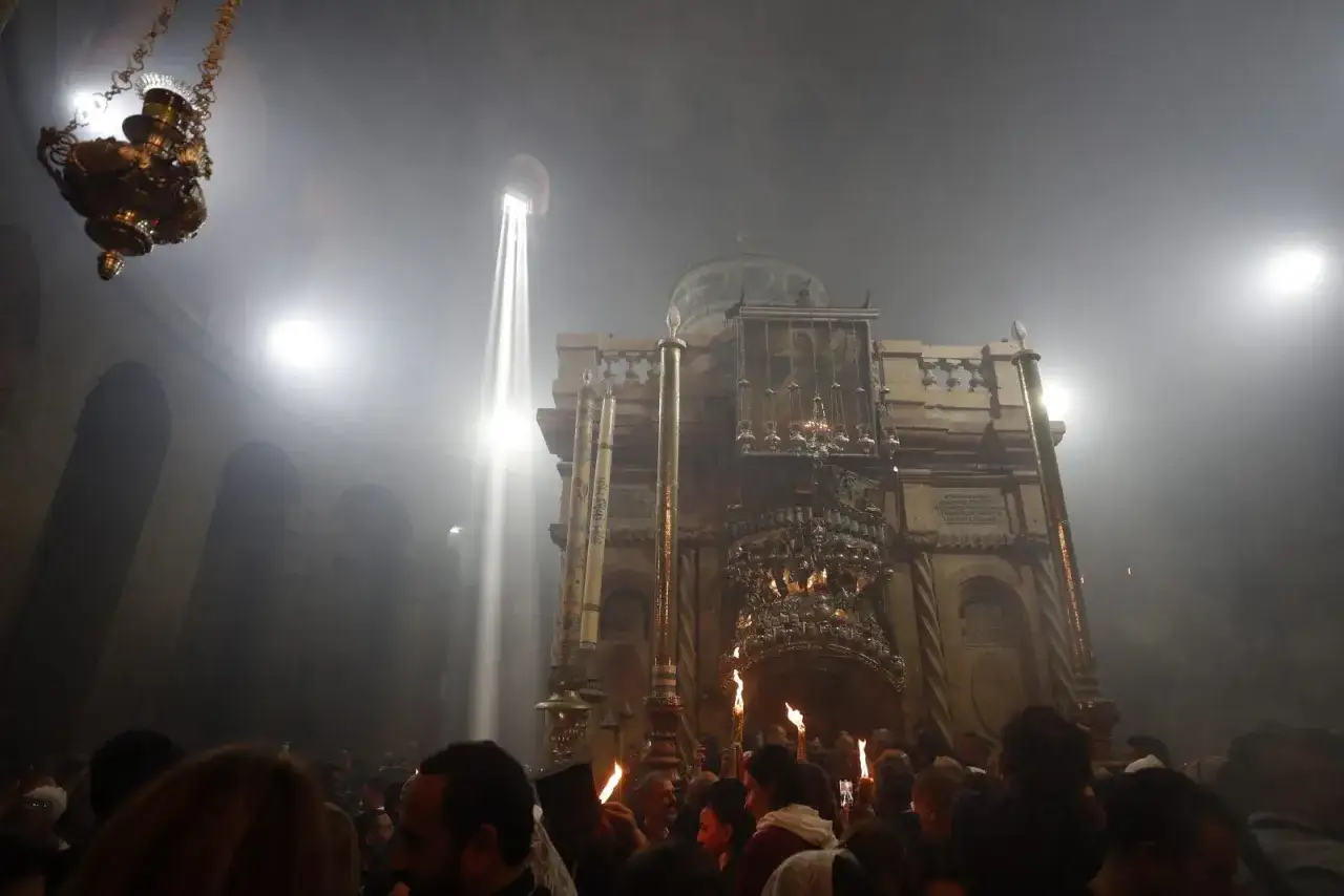 Wnętrze Bazyliki Grobu Pańskiego, wierni przygotowują się do nocnej modlitwy. Promienie światła przebijają się przez dym.