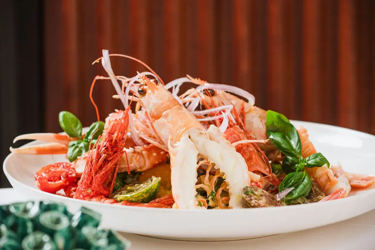 Scampi alla catalana: un piatto colorato con gamberi, pomodorini, cipolla rossa e basilico su un piatto bianco.
