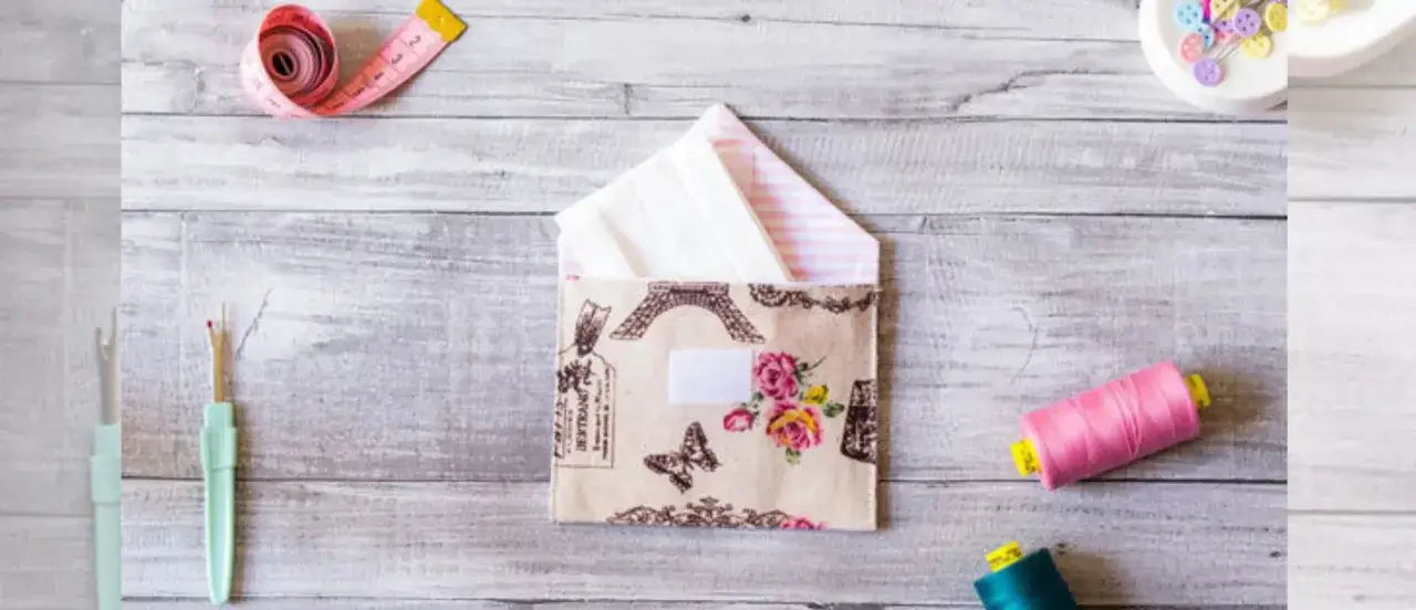 Sobres de tela con diseño de París y flores, junto a hilos, cinta métrica y descosedor.