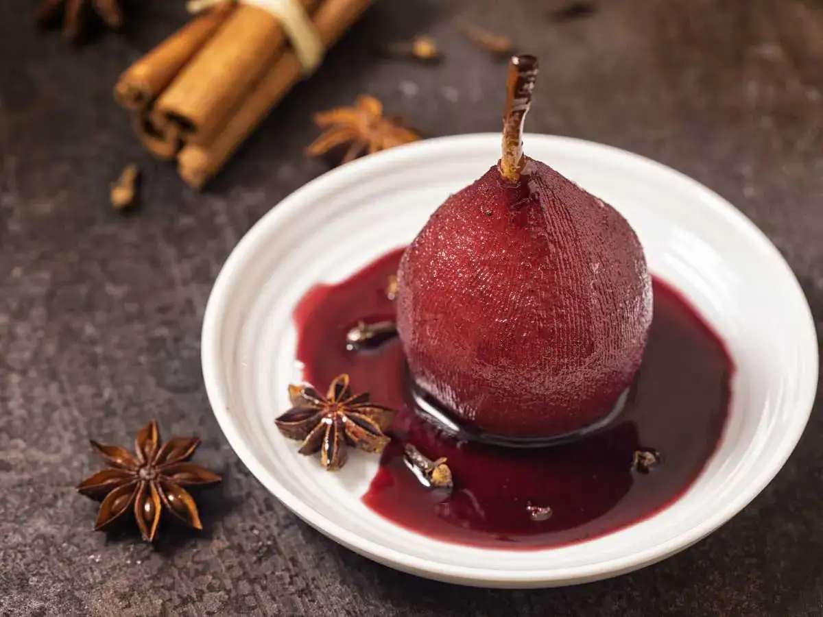 Peras al vino, cocinadas a la perfección, servidas en un plato blanco con anís estrellado y canela.