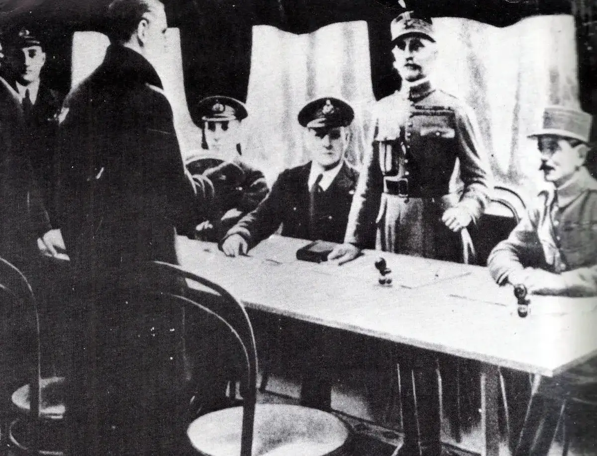 Männer in Uniformen und Zivilkleidung versammeln sich an einem Tisch. Die Szene erinnert an die Unterzeichnung eines wichtigen Dokuments, das vielleicht darüber entscheidet, wer gewann den ersten Weltkrieg.