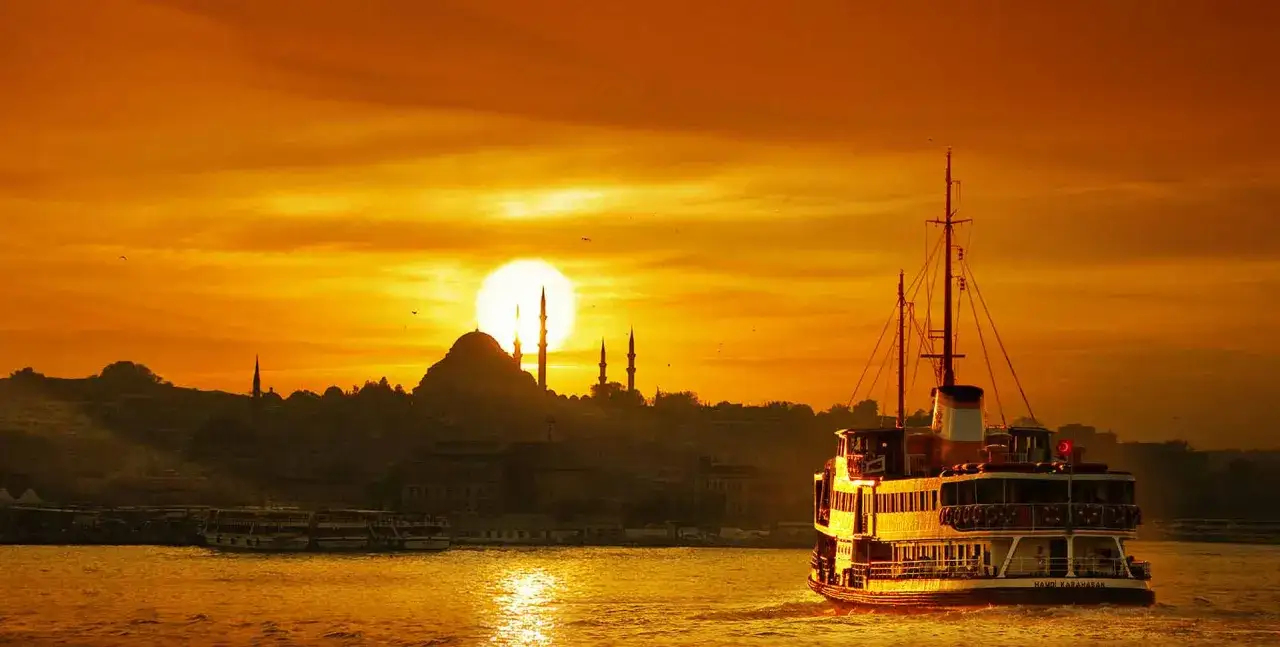 Ein Schiff fährt bei Sonnenuntergang auf dem Bosporus. Die Silhouette von Istanbul mit Moscheen und Minaretten im warmen Licht ist ein unvergesslicher Anblick auf einem Istanbul trip.