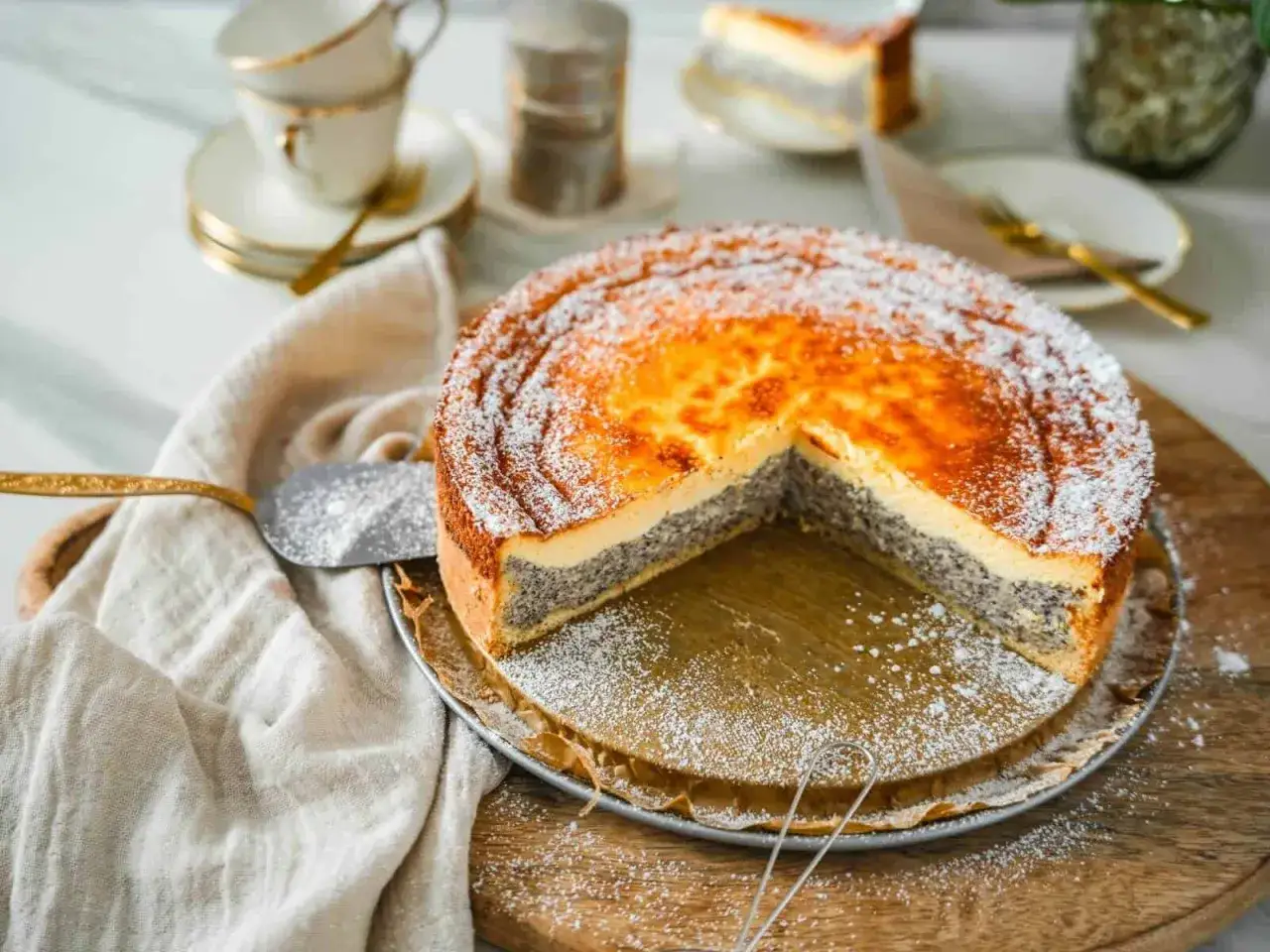 Ein k&ouml;stlicher Mohn Schmand Kuchen, best&auml;ubt mit Puderzucker, wartet darauf, angeschnitten zu werden. Daneben liegen Kaffeetassen.