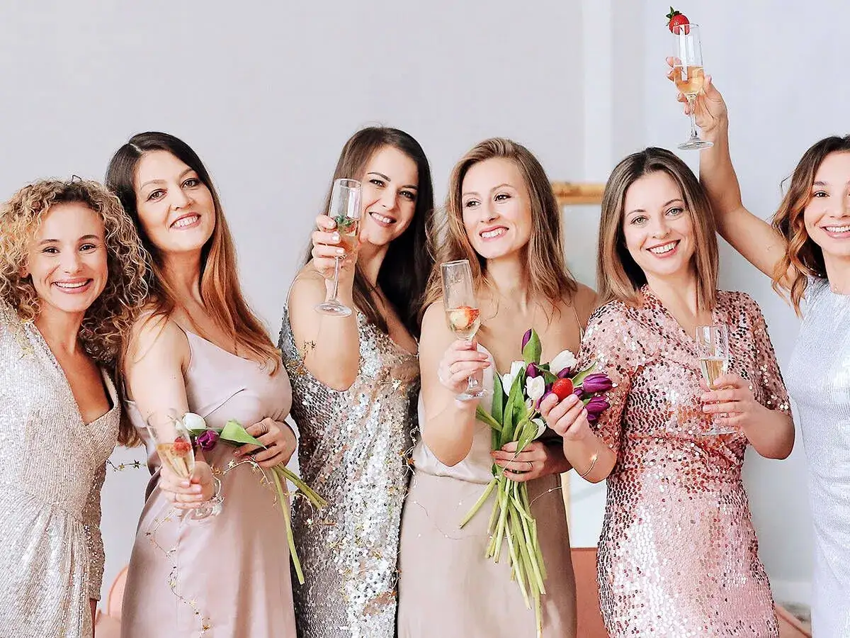 Seis amigas brindan con copas de champán, celebrando juntas. ¡Perfectas ideas para despedidas llenas de brillo y alegría!