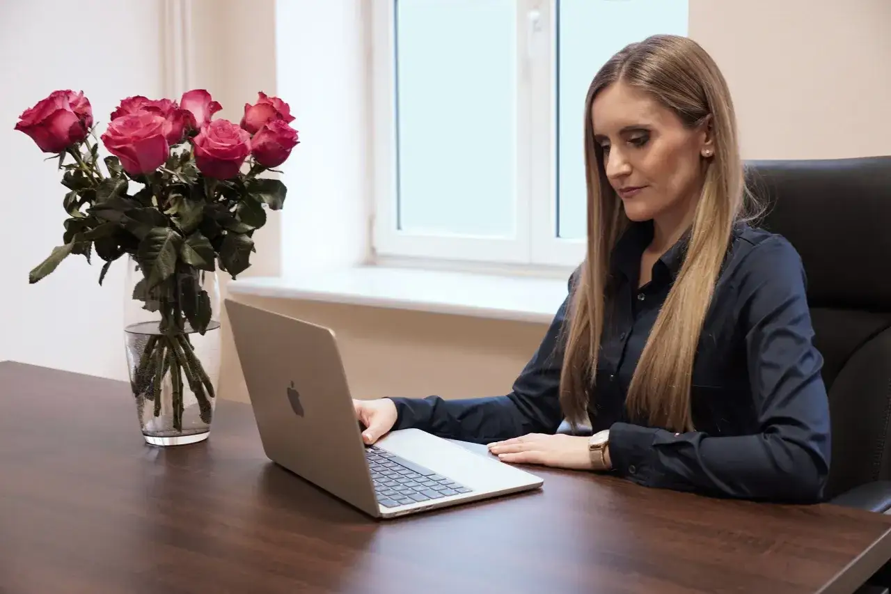 Kobieta w biurze pracuje przy laptopie, obok bukiet róż.