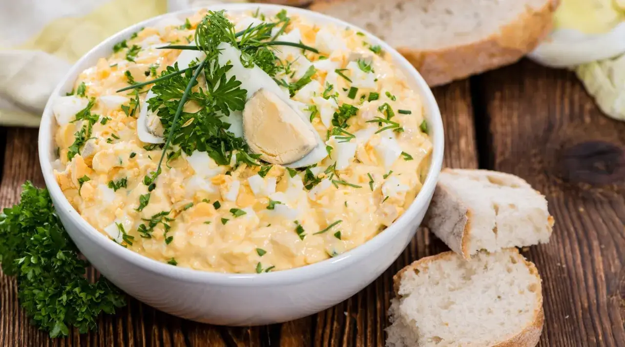 Cremiger eiersalat mit joghurt und gurke, garniert mit frischer Petersilie und Dill. Dazu gibt es rustikales Brot.