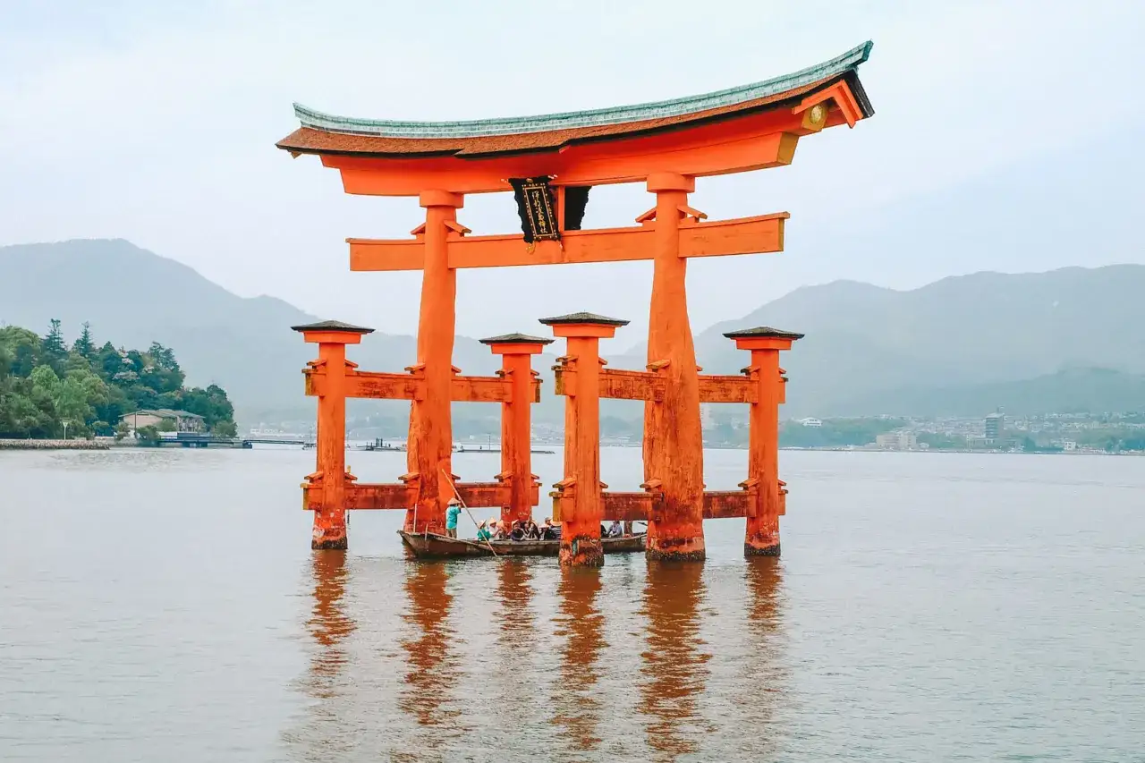 Piękne Japonia widoki: Wielka pomarańczowa brama torii wznosi się z wody, a łodzie z turystami przepływają pod nią.