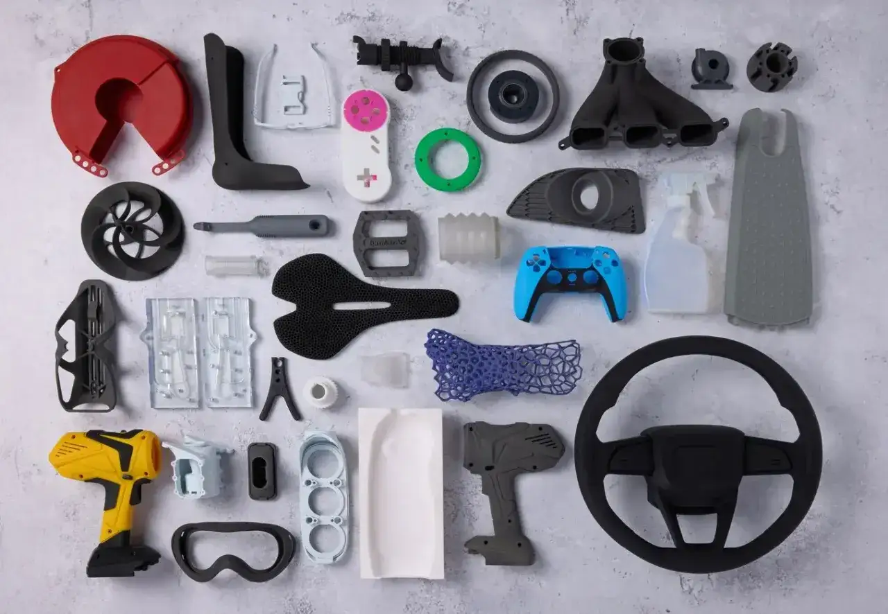 A diverse collection of 3D printing examples, showcasing everything from a yellow drill and blue game controller to a car steering wheel and bicycle saddle.