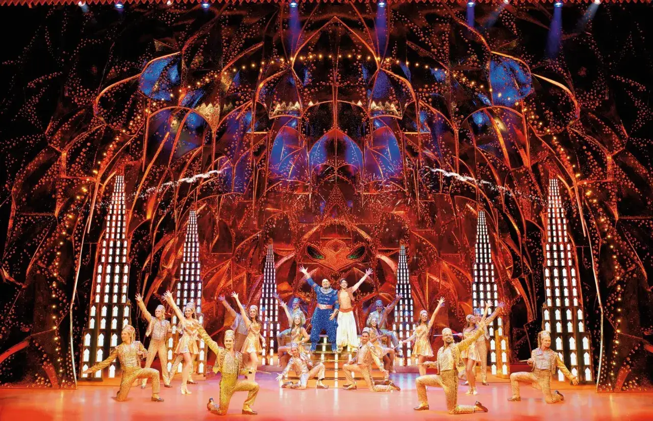 B&uuml;hnenbild mit Darstellern in goldenen Kost&uuml;men und einem blauen Gewand im Zentrum. Ein Spektakel der Musicals Deutschland.