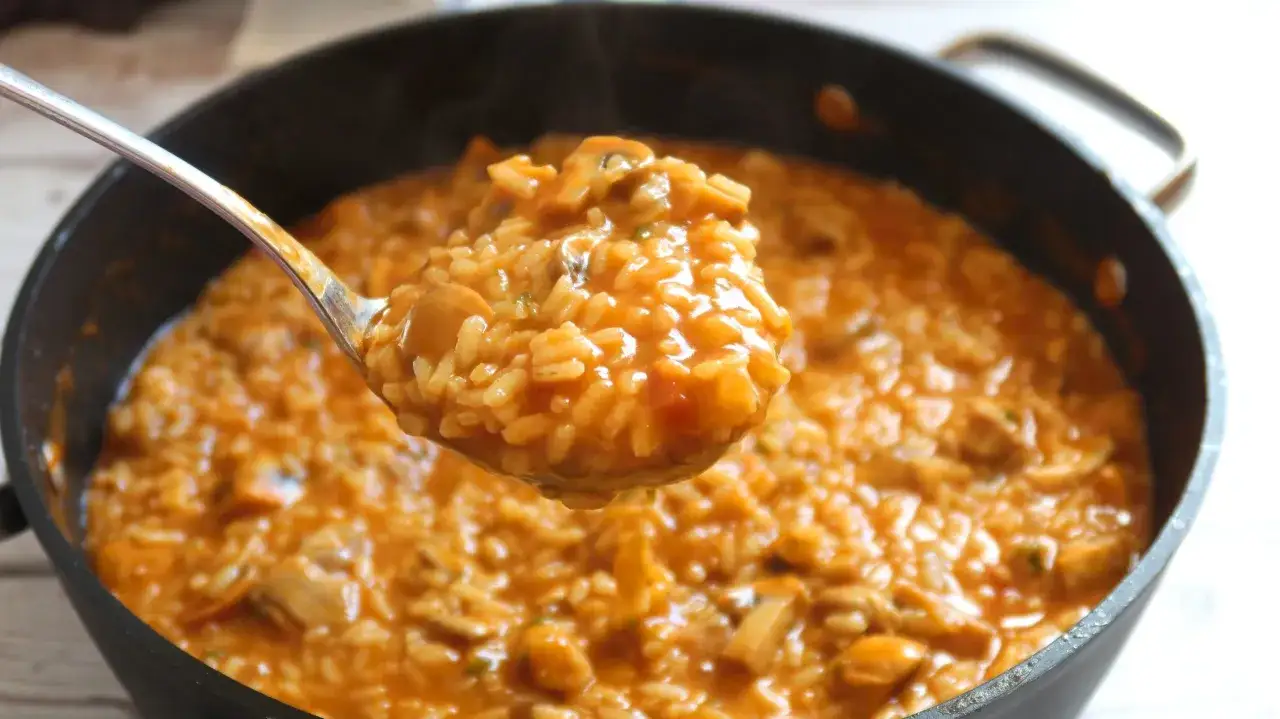 Cuchara llena de arroz meloso con trozos de champiñones y marisco, humeante y listo para servir.