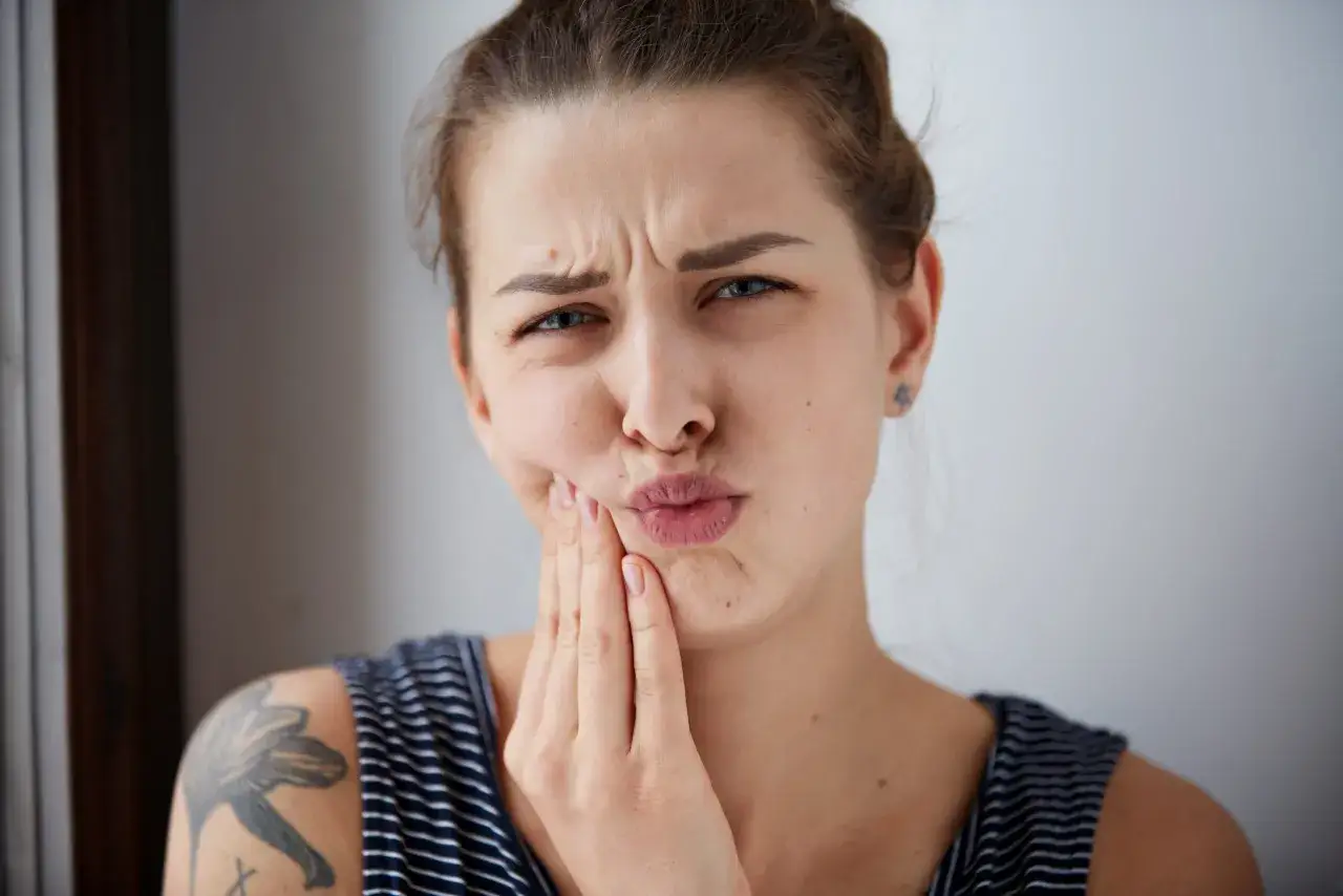 Mujer con cara hinchada por implante dental, frunciendo el ceño y tocándose la mejilla con la mano.