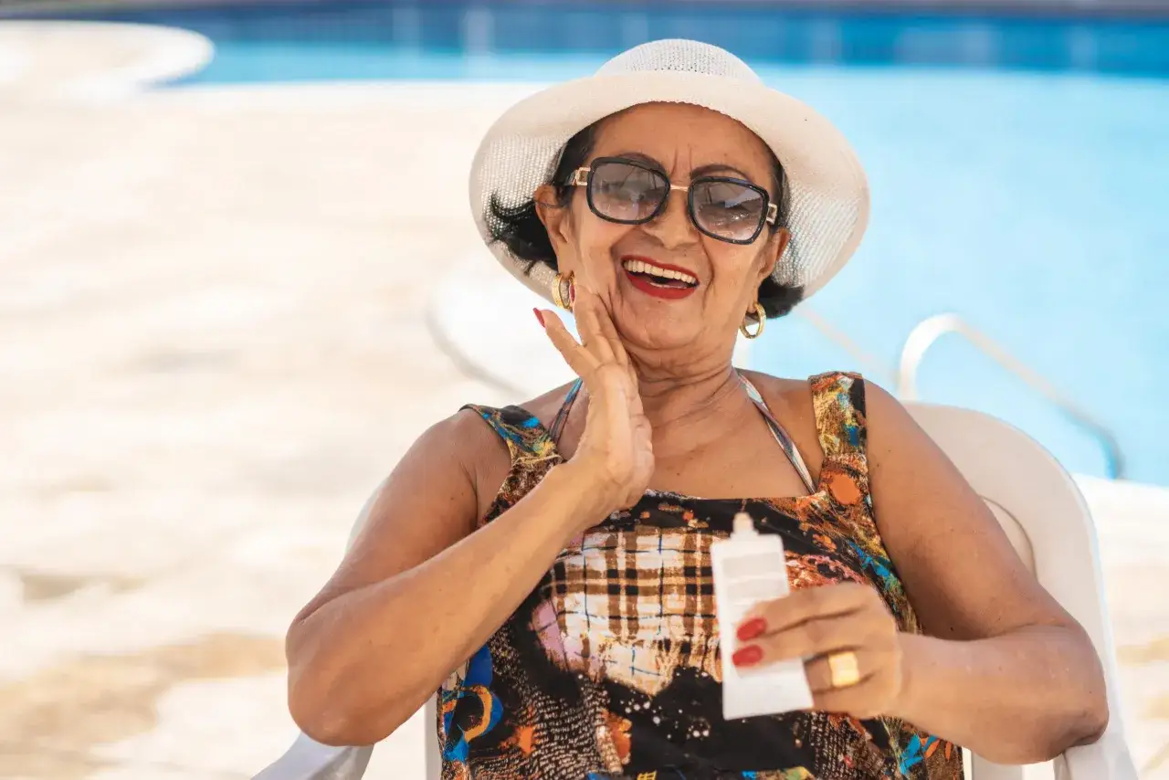 Frau mit Hut und Sonnenbrille h&auml;lt eine Tube Sonnencreme, um eine bessere Haut zu bekommen.