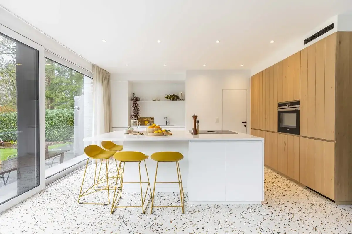 Cuisine moderne avec &icirc;lot blanc, tabourets jaunes vifs et armoires en bois. Parfaites id&eacute;es cuisine pour un espace lumineux et accueillant.