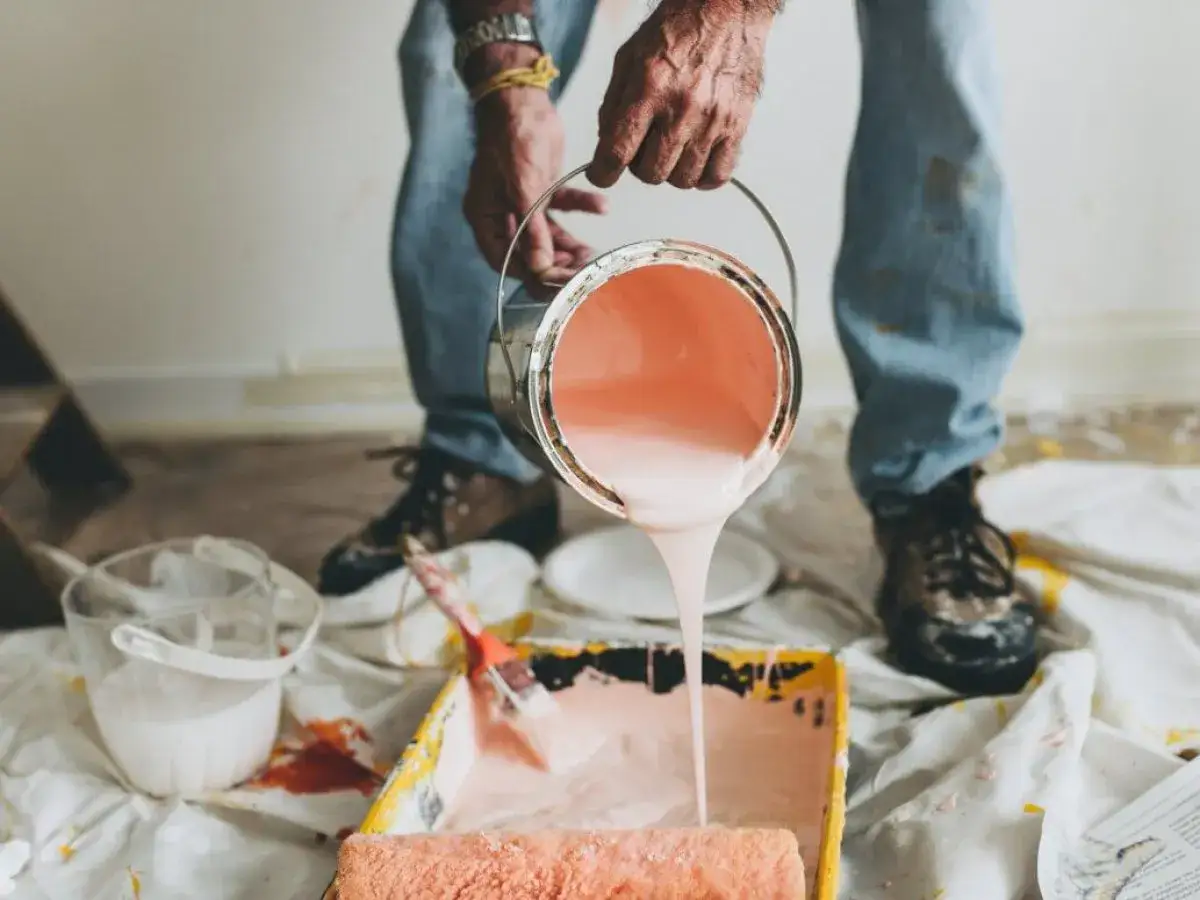 Un uomo versa pittura rosa da un barattolo in una vaschetta per rulli. La pittura pronta all'uso va diluita per ottenere la consistenza perfetta.